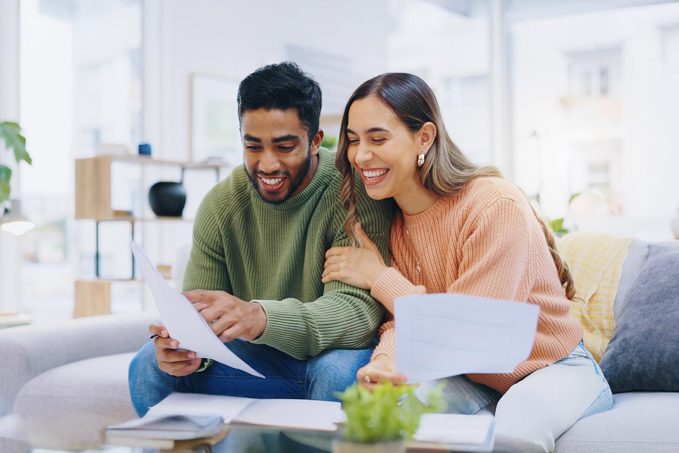 Two people looking over paperwork on a couch. They are both smiling. 