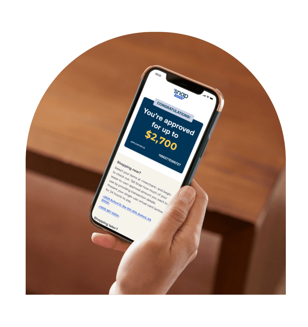A person holding a smartphone displaying a message about an approval for up to $2,700 from Snap Finance. The phone screen shows bold text and logo. The background is a wooden surface.