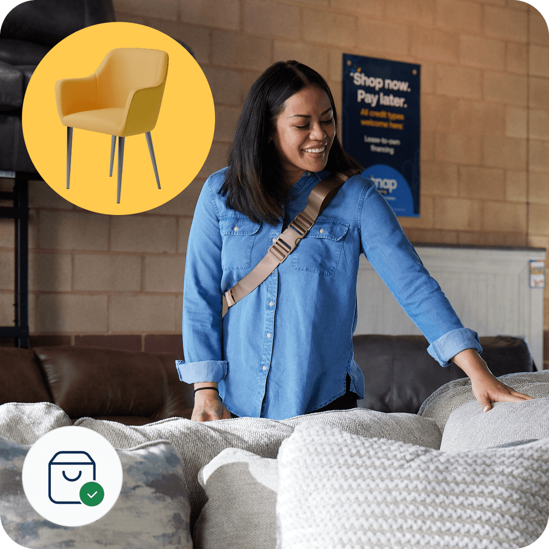 Woman in a denim shirt smiles while touching a sofa in a showroom. A yellow chair icon and shopping app logo are visible.
